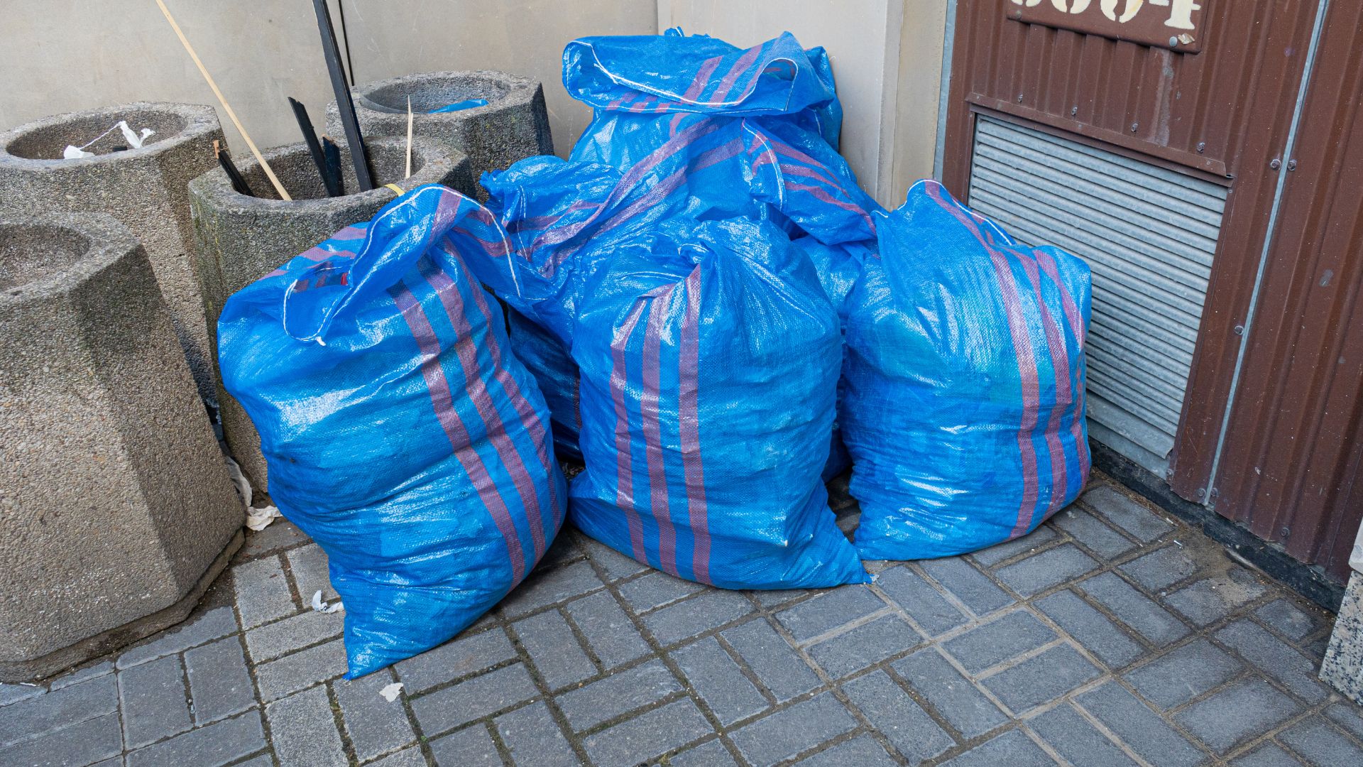 Blue plastic garbage bags with stripes stacked near concrete planters