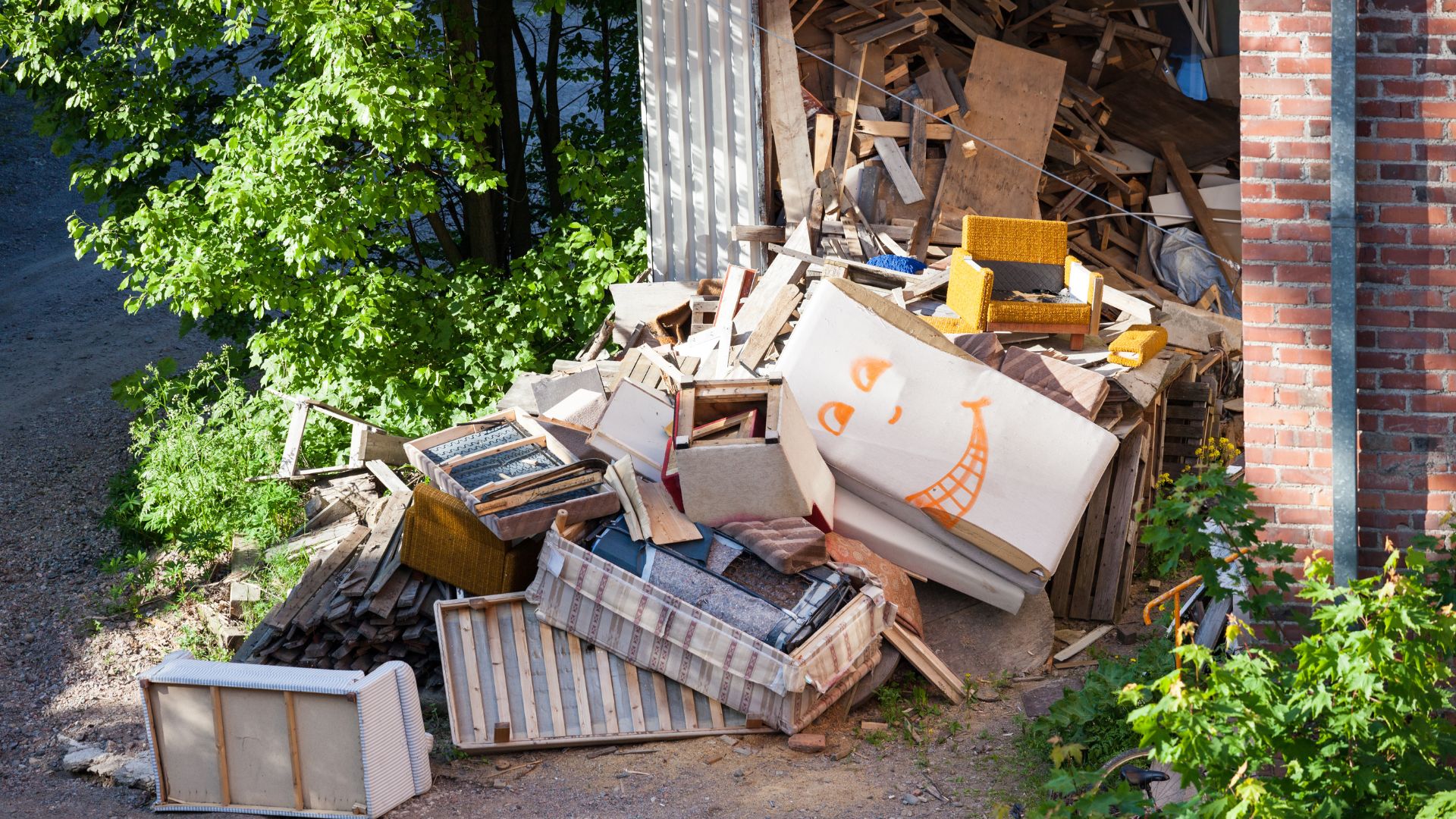 Messy pile of discarded furniture, wood scraps, and debris near brick wall